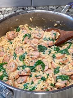 pasta with sausage and spinach in a saucepan on the stove top next to a wooden spoon