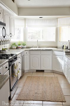 a kitchen with white cabinets and an area rug in front of the stove top oven