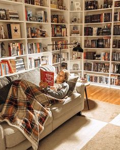 a person laying on a couch with a book in their hand and some bookshelves behind them