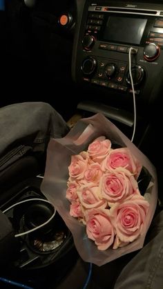 a bouquet of pink roses sitting on top of a bag in front of a car radio