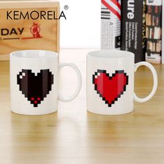 two coffee mugs sitting on top of a wooden table next to a box of books