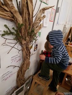 a young boy standing next to a fake tree