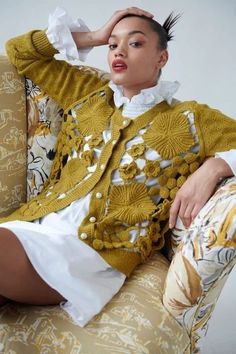 a woman sitting on top of a couch wearing a yellow jacket and white dress shirt