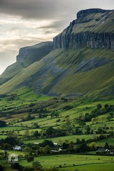 the mountains are covered in lush green grass and there is a house on the far side