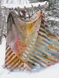 a blanket is hanging on a wooden fence in the snow, with trees behind it