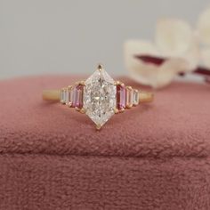 an engagement ring with three stones in it on top of a pink velvet box next to white flowers