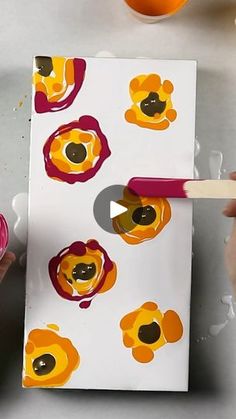 someone is painting flowers on a piece of paper with acrylic paint and a brush