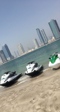 three jet skis are lined up on the beach in front of the city skyline