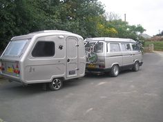 two vans parked next to each other in a parking lot with trees and bushes behind them