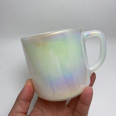 a hand holding a white coffee cup with iridescent paint