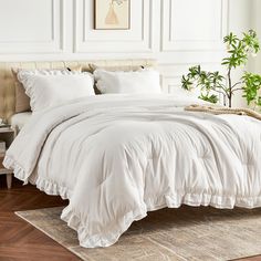 a bed with white comforter and pillows in a room next to a potted plant