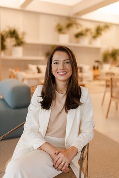 a woman in a white suit sitting on a chair with her legs crossed and looking at the camera