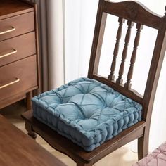 a wooden chair with a blue cushion on top of it next to a bed and dresser