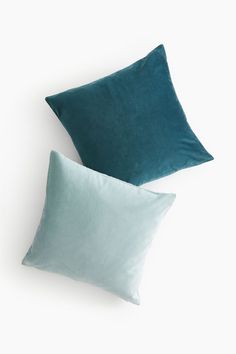 two blue pillows sitting next to each other on top of a white surface with one green pillow