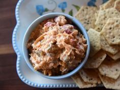 a bowl filled with dip next to crackers on top of a blue and white plate