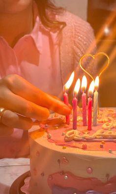 a woman lighting candles on a cake with pink frosting and heart shaped icing