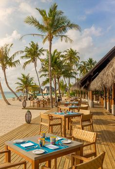 an outdoor dining area on the beach with palm trees and blue tableware set for two