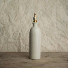 a white bottle with a gold top sitting on a wooden table next to a wall