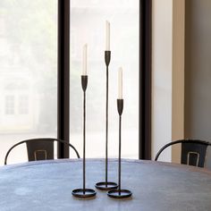 three candles sitting on top of a table next to two black chairs and a window