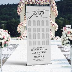 a wedding ceremony sign with flowers on it and the names of the guests in white