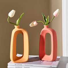 two vases sitting on top of a stack of books with flowers in each one