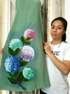 a woman standing next to a green dress with flowers painted on the front and side