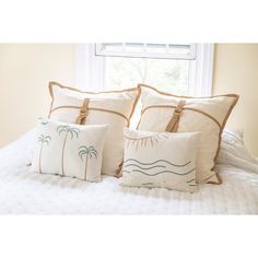 three pillows sitting on top of a bed with white sheets and tan trimmings