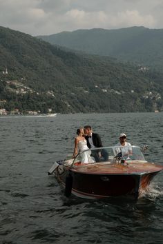 a bride and groom are on the back of a speedboat in the water with mountains in the background