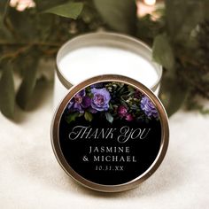 a personalized candle tin with purple flowers on it and greenery in the background