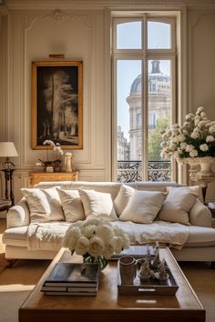 a living room filled with white furniture and flowers on top of a wooden coffee table