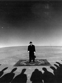 a man standing on top of a rug in the middle of a field with lots of shadows