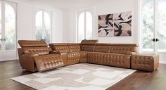 a brown leather sectional sofa sitting on top of a wooden floor next to two windows