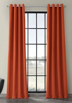 an orange curtain hanging in front of a window with a black chair next to it