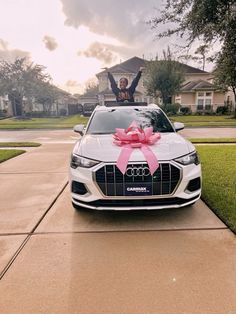 an audi car with a pink bow on the hood parked in front of a house