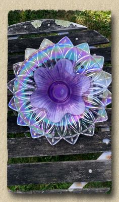 a purple glass flower sitting on top of a wooden bench in front of some grass