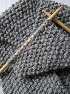 two knitting needles on top of a gray knitted blanket