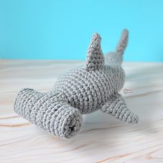 a crocheted gray stuffed animal laying on top of a wooden table next to a blue wall