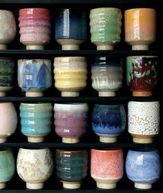 many different colored bowls lined up in a row on a shelf with black shelves behind them