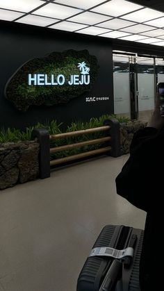 a woman taking a photo of herself with her cell phone in front of the hello jeju sign