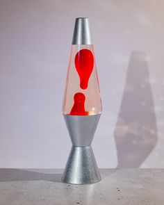 a silver and red vase sitting on top of a cement floor next to a white wall