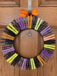 a wreath made out of clothes pins and orange ribbon hanging on the front door with an orange bow