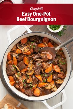 a pot filled with beef and carrots on top of a table next to bread