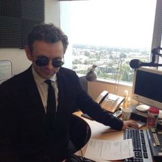 a man sitting at a desk in front of a computer monitor and keyboard wearing sunglasses