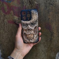 a person holding up a phone case with an image of a demon face on it