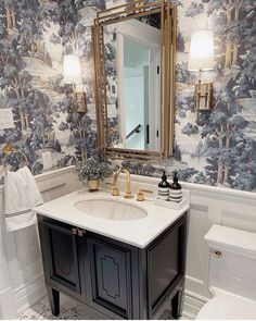 a bathroom with blue and white wallpaper, gold accents and a mirror above the sink