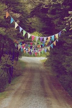 a dirt road surrounded by trees and bunting with colorful flags hanging from the sides