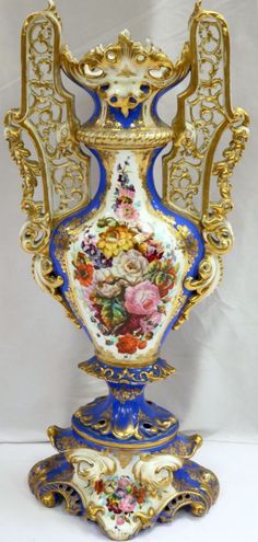 an ornate blue and gold vase with flowers on it's sides, sitting against a white background