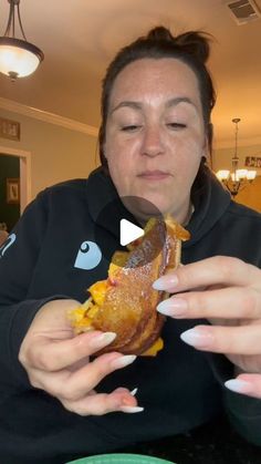 a woman is eating a large sandwich at the table