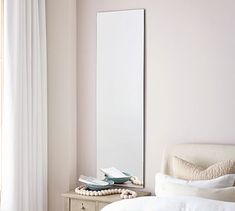 a mirror sitting on top of a wooden dresser next to a white bed in a bedroom