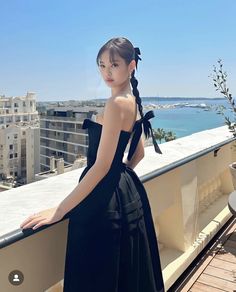 a woman standing on top of a balcony next to the ocean with buildings in the background